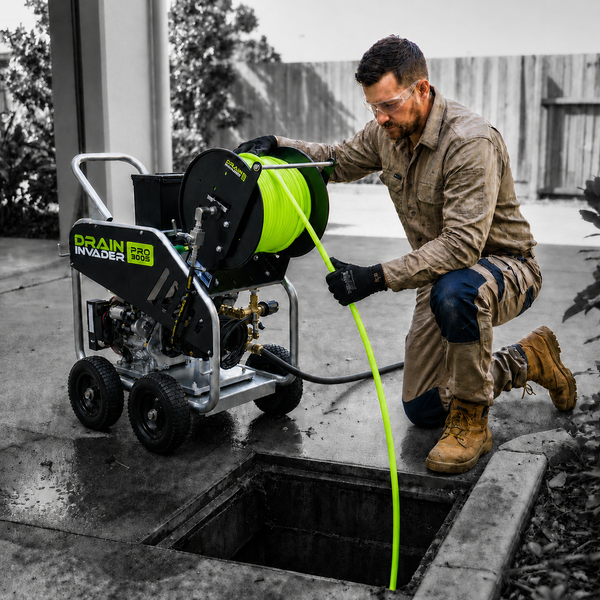 A man kneels beside an open drain while using a Drain Invader Pro 3005 hydro-jetter
