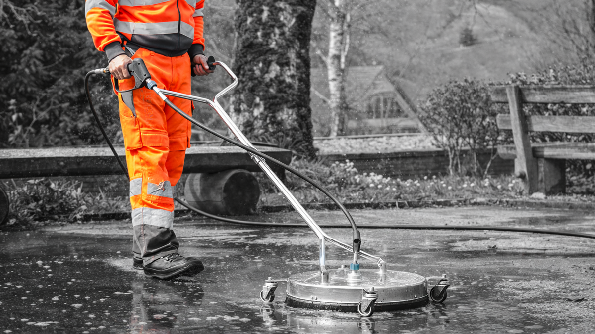 Person using a pressure washer surface cleaner on a concrete surface with a blurred background