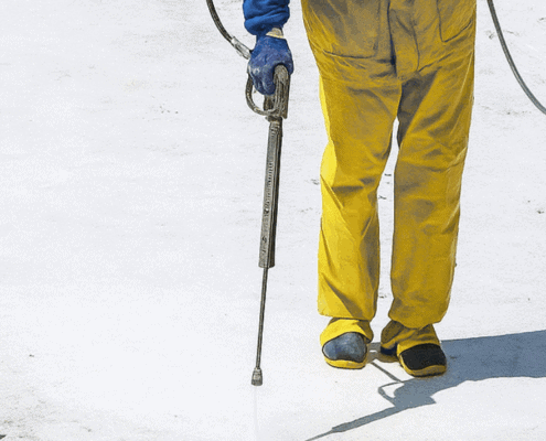 man wearing winter safety equipment pressure washing in the snow