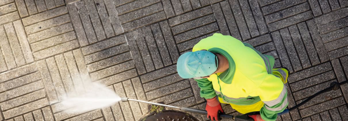 Worker cleaning a street sidewalk with high pressure water jet machine on sunny day. Copy space. Top view