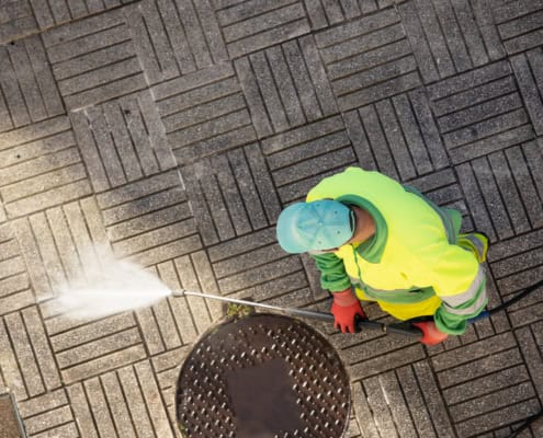 Worker cleaning a street sidewalk with high pressure water jet machine on sunny day. Copy space. Top view
